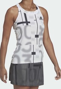 Vit atletisk tanktopp med svarta geometriska mönster, kombinerad med en mörkgrå kjol som har varierade texturer och subtila prickmönster.