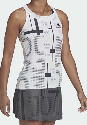 Débardeur de sport blanc avec des motifs géométriques noirs, associé à une jupe grise foncée présentant des textures variées et des motifs de points subtils.