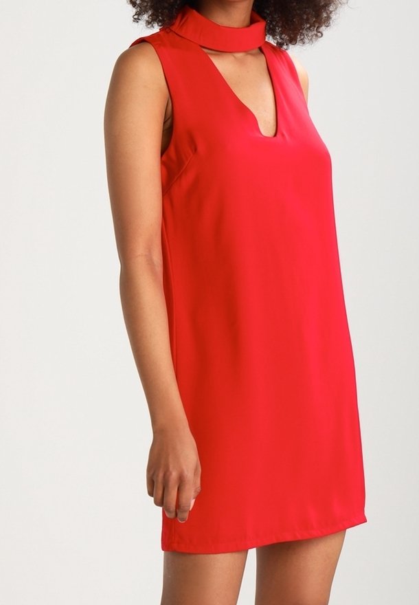 Robe rouge sans manches avec un décolleté en V profond et un col montant. Texture lisse, silhouette droite, et longueur jusqu'aux genoux.