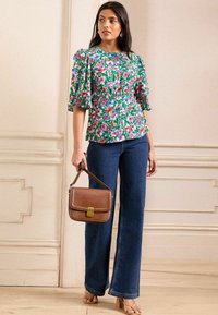 Ziedu krekls ar pūkainām piedurknēm zaļā, rozā un zilā krāsā. Apvienots ar tumši ziliem platiem džinsiem un brūnu teksturētu rokassomu.