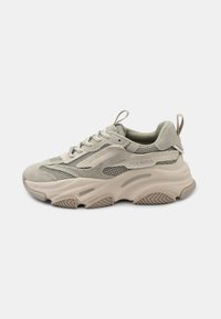 Sneaker atletiche grigio chiaro realizzate in materiali mesh e suede, con suola in gomma spessa, un evidente motivo di battistrada e dettagli di marca sul lato.