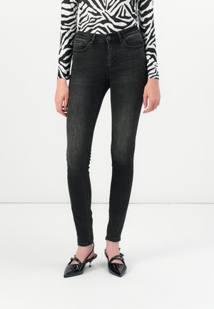 Black skinny jeans with a slightly faded finish, featuring a five-pocket design and a button closure. Paired with pointed black patent heels.