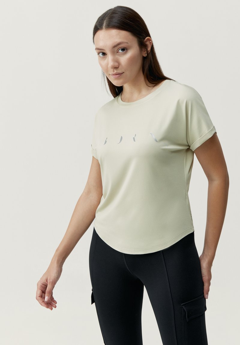 Lichtgroene top met korte mouwen en een ronde halslijn, met een gebogen zoom, voorzien van een eenvoudige grijze grafische afbeelding op de borst, gedragen met zwarte leggings.
