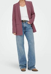 Lavendel Blazer mit scharfen Revers, kombiniert mit einem weißen T-Shirt und hoch taillierten, hellblauen weit geschnittenen Jeans. Auffälliger goldener Gürtelakzent.