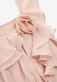 Blouse rose clair avec un design volé et un accent en rose. Fabriquée en tissu doux et texturé, elle possède des couches délicates et fluides.