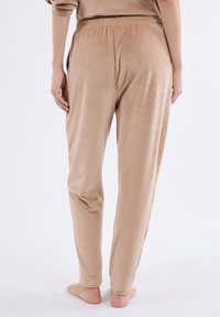 Beige geribde broek met een elastische tailleband, taps toelopend ontwerp en een zachte textuur. Zichtbare naden en gelijkmatig verdeelde verticale lijnen.