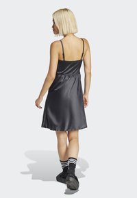 Black satin dress with adjustable spaghetti straps, elastic waistband, and a flared silhouette, paired with black shoes and striped socks.