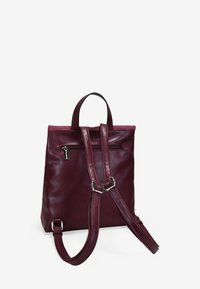 Mochila de piel burdeos con correas ajustables, bolsillo trasero con cremallera y un robusto asa superior. Textura lisa y diseño minimalista.