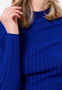 Niebieski sweter w prążki z wysokim kołnierzem, ozdobiony fakturalnym wzorem ściegów. Rękawy są długie i dopasowane, z gładkim wykończeniem tkaniny.