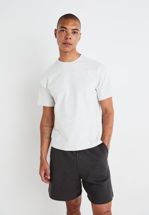 T-shirt gris à col rond avec manches courtes, fabriqué dans une matière douce. Porté avec un short sombre, doté d'une coupe décontractée et d'une taille à cordon.