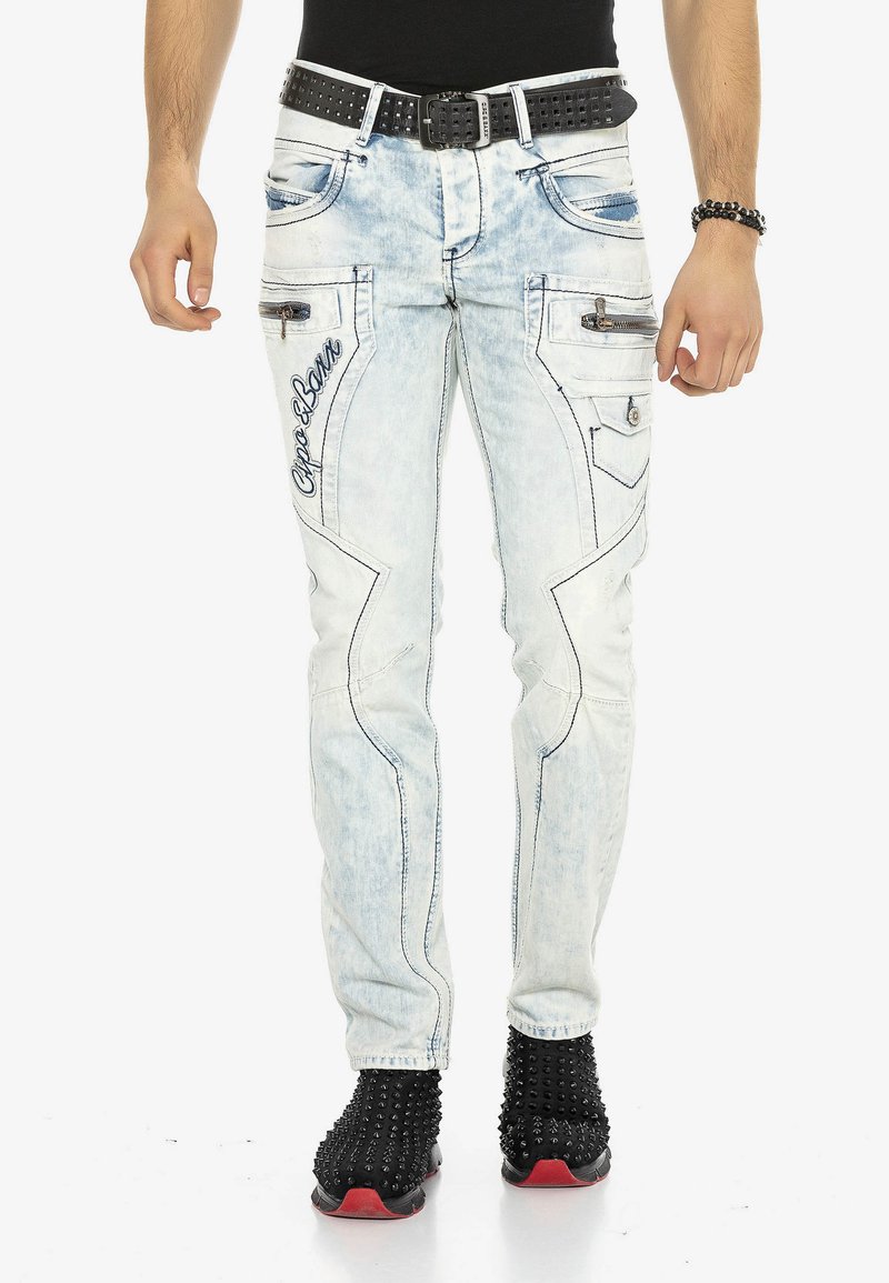 Hellblaue Denim-Jeans mit schlanker Passform, die gestickte Akzente, Reißverschlusstaschen und ein besticktes Logodetail aufweisen. Getragen mit einem schwarzen Nieten-Gürtel.
