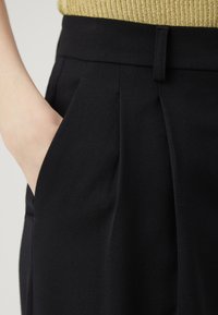 Μαύρο tailored παντελόνι από υφασμάτινη ύφανση, με πιέτες μπροστά και πλαϊνές τσέπες, σε συνδυασμό με ένα ριγέ χρυσό τοπ.