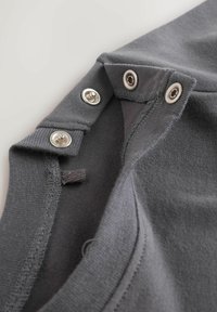 Szara tkanina o gładkiej fakturze z srebrnymi zatrzaskami po bokach. Wzór obejmuje czysty, nowoczesny dekolt oraz detale szwów.