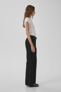 Camiseta blanca ajustada combinada con pantalones de pierna ancha negros de cintura alta. La modelo lleva tacones negros de punta y accesorios mínimos.
