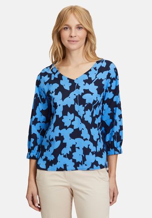 Blue floral-patterned blouse with a V-neck and three-quarter sleeves, made of lightweight fabric against a navy background.