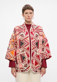 Színes, oversize, mintás dzseki piros, rózsaszín, fekete és narancssárga háromszögekkel. Texturált anyagból készült, két első zsebbel rendelkezik.