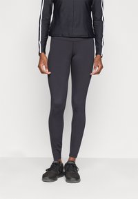 Leggings neri in un design aderente con una texture liscia e strisce laterali bianche. Abbinati a una giacca nera e scarpe da ginnastica nere.