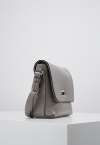 Szara skórzana torba na ramię z klapą i srebrnymi akcentami, z odpinanym paskiem na ramię i gładką teksturą.