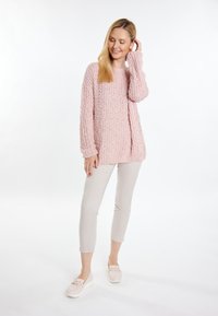 Maglione oversize rosa chiaro con trama a maglia, maniche lunghe e scollo a giro, abbinato a pantaloni fitted beige e scarpe slip-on chiare.
