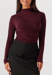 Bordeaux lange mouwen top met geraffineerde details, gecombineerd met een zwarte rok met twee voorzakken en een gladde textuur.