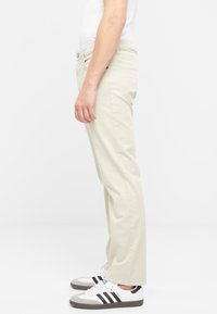 Pantalones rectos beige hechos de una mezcla de algodón, con bolsillos laterales y traseros, de textura lisa y ajuste clásico. Combinados con zapatillas blancas.