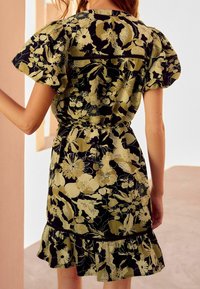 Robe à motifs floraux avec manches courtes bouffantes, taille cintrée et ourlet à volants. Couleurs : noir, vert et crème.