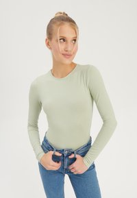 Light green long-sleeve top with a round neckline, paired with high-waisted blue jeans. Material appears soft and smooth.