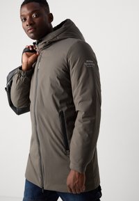 Lightweight, hooded parka in olive green, featuring a zip closure, elastic cuffs, and side pockets with black zippers. Ecoalf branding displayed.