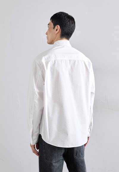 Camisa blanca de manga larga con un sutil patrón de puntos, dobladillo redondeado, cuello abotonado y puños. Combinando con pantalones grises con textura.