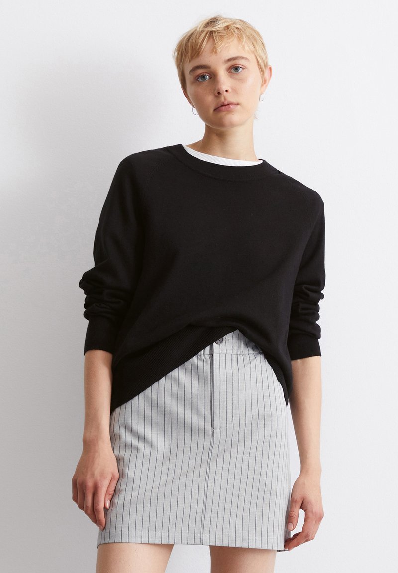 Μαύρο πλεχτό πουλόβερ με στρογγυλή λαιμόκοψη, συνδυασμένο με γκρι φούστα με ρίγες. Το πουλόβερ διαθέτει χαμηλωμένα μανίκια και ribbed τελείωμα.