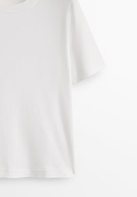 T-shirt bianca a maniche corte in morbido cotone con scollo rotondo e vestibilità standard. Texture liscia, senza motivi o dettagli aggiuntivi.