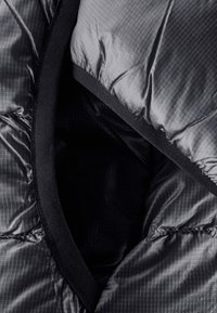 Doudoune noire avec une texture lisse et brillante, présentant un motif à rayures diagonales et un bord élastique noir autour de l'ouverture.