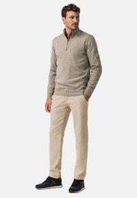 Hellgrauer Pullover mit halbem Reißverschluss, kombiniert mit beigen Hosen und schwarzen Sportschuhen. Weiche Textur, legere Passform und keine sichtbaren Muster.