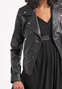 Mustat nahka-motopaita, jossa on hopeiset yksityiskohdat, etuvetoketju ja tiukka siluetti, yhdistettynä mustaan mekkoon alla.