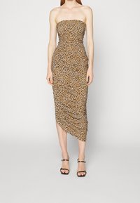 Robe midi sans manches en imprimé léopard avec détail froncé, ourlet asymétrique et silhouette ajustée. Portée avec des sandales à talons noires.