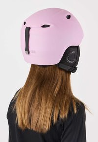 Pink ski helmet with matte finish, black padding, adjustable strap, and ventilation holes on top and sides. Visible back clip for secure fit.