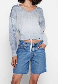 Pull tricot bleu clair avec col en V et manches longues, associé à un short en denim bleu moyen avec ourlet effiloché et poches.
