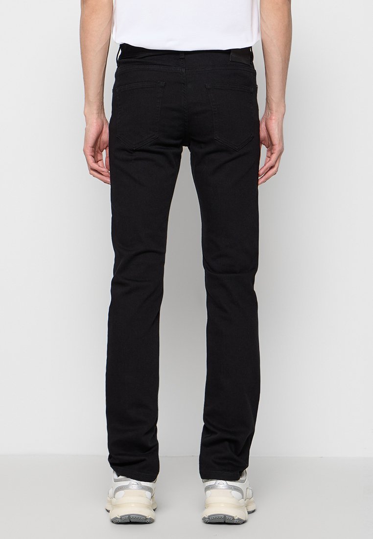Czarne dżinsy o slim fit, z symetrycznymi tylnymi kieszeniami i gładką fakturą, zestawione z jasnymi sneakersami.