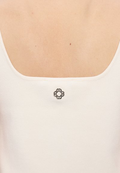 Valge tank top ruudukujulise dekolteega, mille taga on väike must lilleembleem. Sile tekstuur ja moodustav disain.