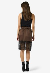 Brun sateng midi-skjørt med svart blonderkant ved kanten. Har elastisk midjebånd og er kombinert med svarte ankelstøvler.