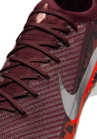 Chaussure de sport tricotée bordeaux avec lacets foncés, logo Nike swoosh argenté, et détail de semelle à motif rouge et noir.