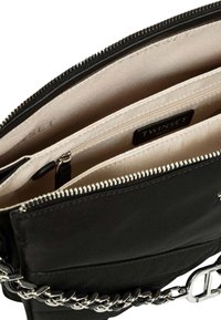 Borsa a tracolla nera con catena argentata, dotata di chiusura con zip, interno beige e molteplici tasche per l'organizzazione.