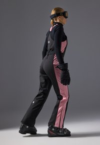 Zwart-roze skikleding met een aansluitend ontwerp, gemaakt van waterdicht materiaal; bevat een harnas, handschoenen en skischoenen.
