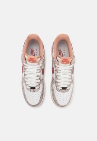 Nike Air Force 1 sneakers with a white and textured beige upper, red accents, and white laces. Features perforated toe and padded collar.