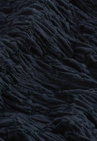 Tissu texturé foncé avec des zones froncées et de petites ouvertures semblables à de la dentelle créant une surface à motifs et tactile.
