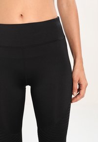 Czarne legginsy sportowe z wysokim stanem, z teksturowanymi akcentami po bokach i dopasowanym krojem, wykonane z elastycznego materiału.