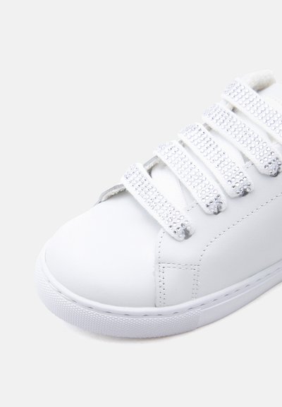 Άσπρο αθλητικό παπούτσι με πέντε λουριά βέλκρο, το καθένα διακοσμημένο με μικρές, λαμπερές ασημένιες καρφίτσες, που δείχνει τις λεπτομέρειες από το μπροστινό και το πλάι.