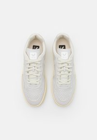 Γκρι σουέτ αθλητικά παπούτσια με διατρήσεις, υφασμάτις χορδές και λευκή ετικέτα λογότυπου στη γλώσσα. Λαστιχένια σόλα με ελαφριά χρωματική αντίθεση.