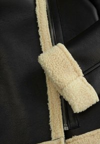 Czarna skórzana kurtka z kremowym futrzanym wykończeniem wzdłuż zamka błyskawicznego i kołnierza, z miękką teksturą kontrastującą z gładką powierzchnią.