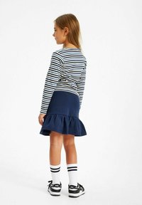 Randig långärmad skjorta i marinblått och vitt, i kombination med en mörk marinblå kjol med utsvängd nederkant. Vita strumpor med svarta ränder och svarta sneakers.